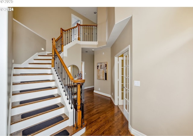 stairway with french doors, a towering ceiling, baseboards, and wood finished floors