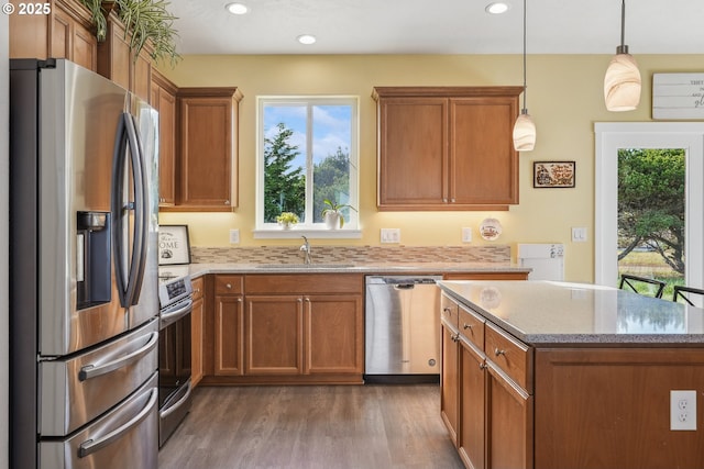 kitchen with sink, light stone counters, hanging light fixtures, appliances with stainless steel finishes, and hardwood / wood-style floors