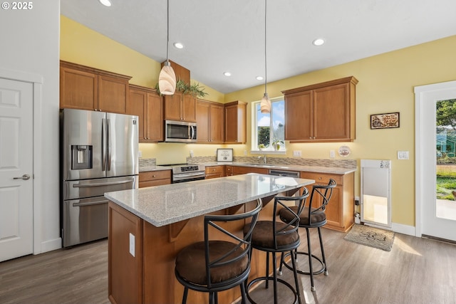 kitchen with pendant lighting, appliances with stainless steel finishes, a center island, light stone counters, and vaulted ceiling