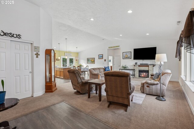 living area with a stone fireplace, light colored carpet, vaulted ceiling, light wood-type flooring, and baseboards
