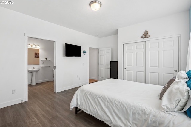 bedroom featuring a sink, baseboards, ensuite bathroom, dark wood-type flooring, and a closet