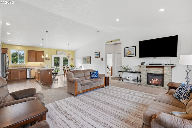 living room with sink, a fireplace, a textured ceiling, vaulted ceiling, and light wood-type flooring