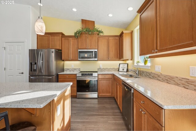 kitchen with light stone countertops, appliances with stainless steel finishes, a sink, brown cabinetry, and dark wood-style floors