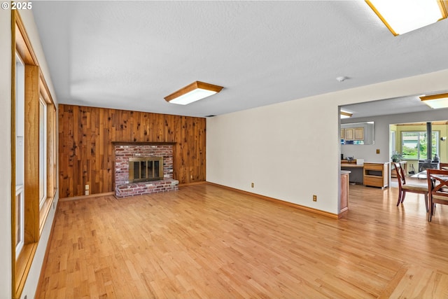 unfurnished living room featuring wooden walls, light wood-style flooring, a textured ceiling, and baseboards