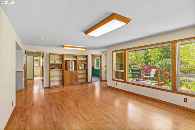 unfurnished living room with light wood-style floors, a healthy amount of sunlight, and baseboards