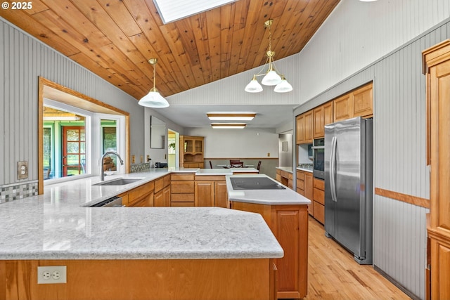 kitchen with a sink, light wood-style floors, stainless steel appliances, decorative light fixtures, and a peninsula