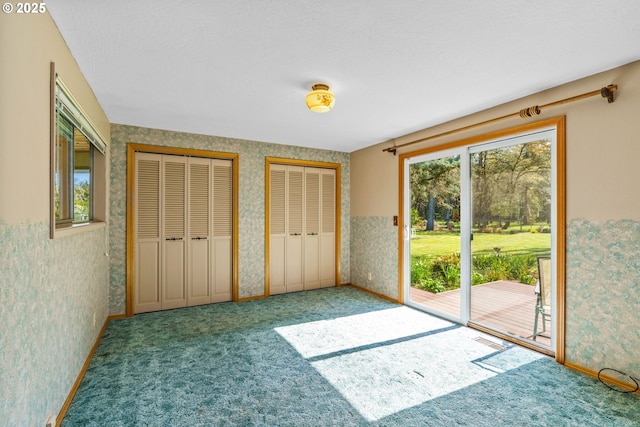 unfurnished bedroom featuring two closets, carpet flooring, access to exterior, and wallpapered walls