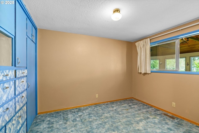 carpeted empty room with baseboards, a textured ceiling, and visible vents
