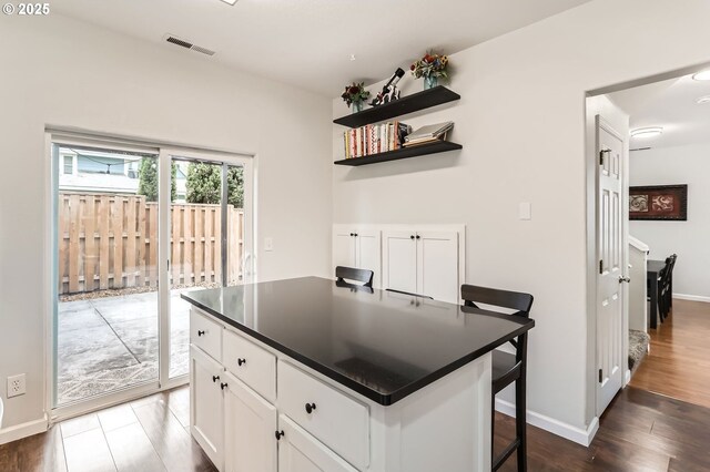 kitchen with visible vents, wood finished floors, dark countertops, baseboards, and white cabinets