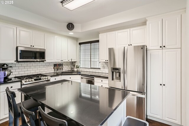 kitchen with tasteful backsplash, white cabinets, dark countertops, and stainless steel appliances