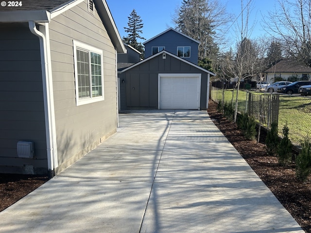 view of side of home with driveway, a detached garage, an outbuilding, fence, and board and batten siding