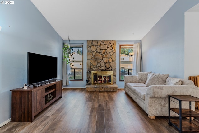 living room with dark hardwood / wood-style flooring, a stone fireplace, and vaulted ceiling