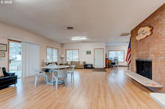 14996 SE Caruthers Ct, Portland, OR 97233 - dining room featuring light wood-style flooring, plenty of natural light, a brick fireplace, and a textured ceiling