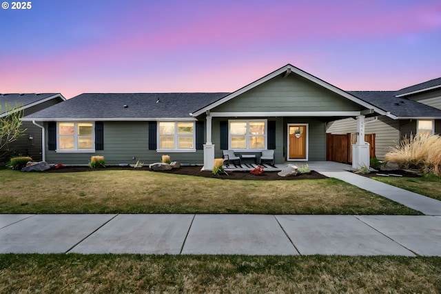 ranch-style house featuring a shingled roof, a porch, and a front yard