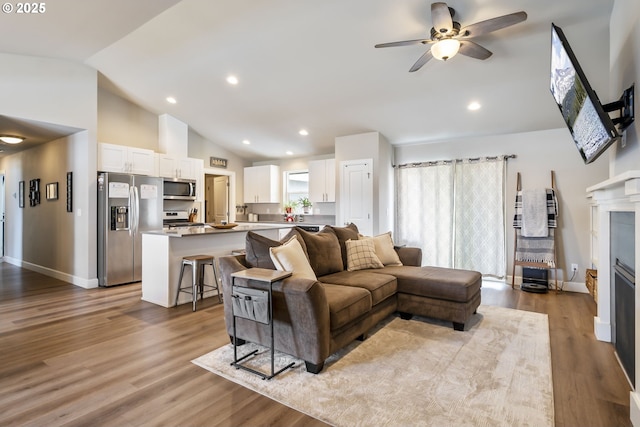 living room with ceiling fan, a fireplace, wood finished floors, baseboards, and high vaulted ceiling