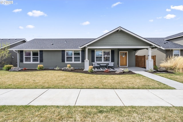 ranch-style house with roof with shingles, fence, a porch, and a front lawn