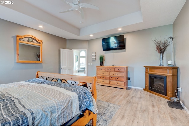 bedroom with ceiling fan, light hardwood / wood-style floors, and a tray ceiling