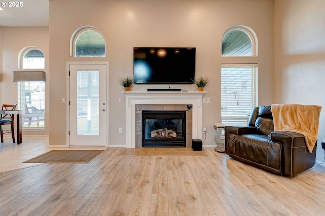 living room featuring a healthy amount of sunlight, a tile fireplace, light hardwood / wood-style flooring, and a high ceiling