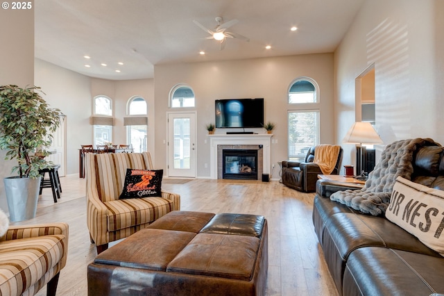 living room featuring ceiling fan, a towering ceiling, a fireplace, and light wood-type flooring