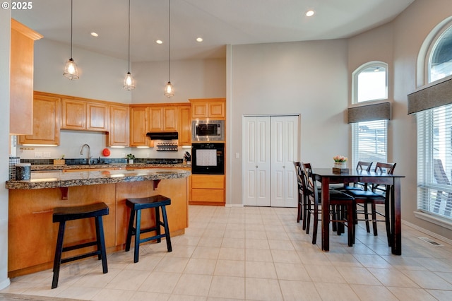 kitchen featuring sink, dark stone countertops, stainless steel microwave, black oven, and a high ceiling