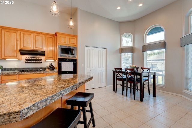 kitchen with pendant lighting, light tile patterned floors, a breakfast bar, a high ceiling, and black appliances