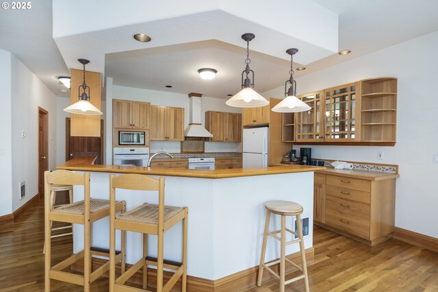 110 SW 61st St, South Beach, OR 97366 - kitchen with white appliances, wall chimney exhaust hood, baseboards, a kitchen bar, and a peninsula