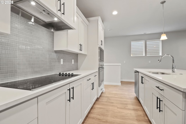 kitchen featuring pendant lighting, wall chimney range hood, sink, appliances with stainless steel finishes, and white cabinets