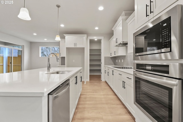 kitchen featuring sink, a kitchen island with sink, hanging light fixtures, stainless steel appliances, and white cabinets