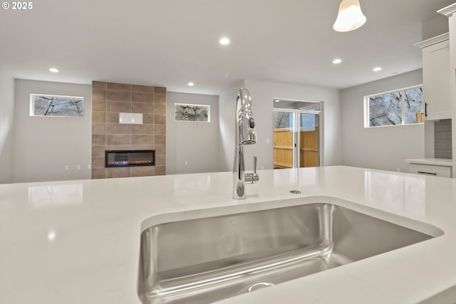 kitchen featuring a tile fireplace, white cabinetry, and sink