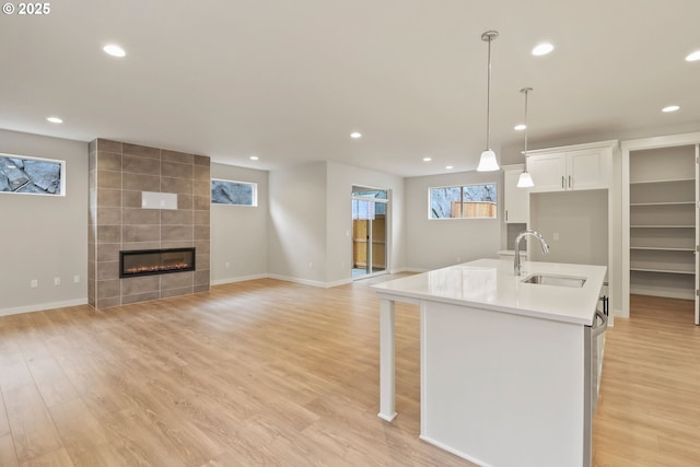 kitchen with a tile fireplace, an island with sink, sink, white cabinets, and hanging light fixtures