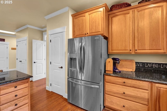 kitchen featuring dark stone countertops, stainless steel fridge, wood finished floors, and crown molding