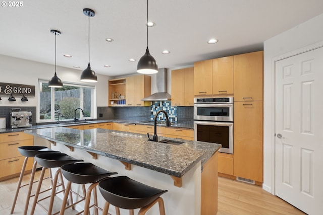 kitchen featuring double oven, sink, light brown cabinets, and wall chimney range hood