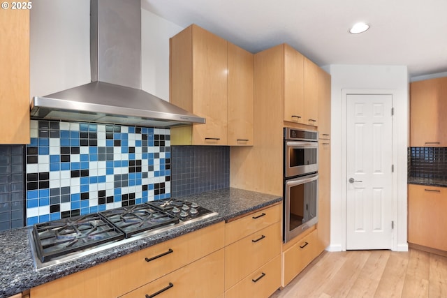 kitchen featuring light wood-type flooring, wall chimney range hood, backsplash, stainless steel appliances, and light brown cabinetry
