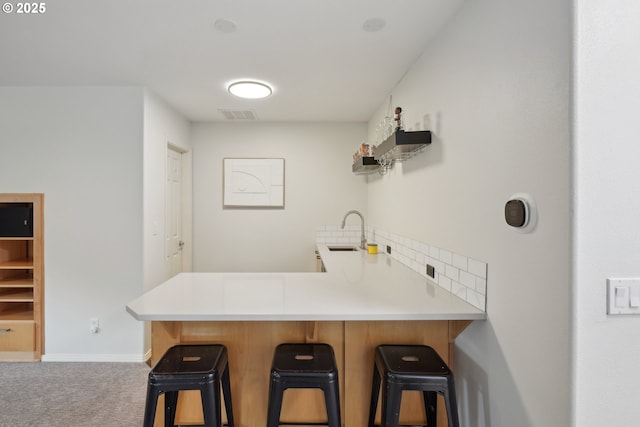 kitchen with sink, a kitchen breakfast bar, carpet, tasteful backsplash, and kitchen peninsula