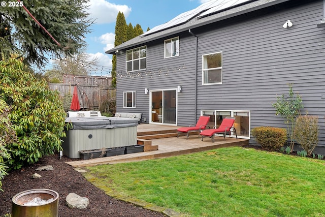 rear view of house featuring a wooden deck, a hot tub, a yard, fence, and solar panels