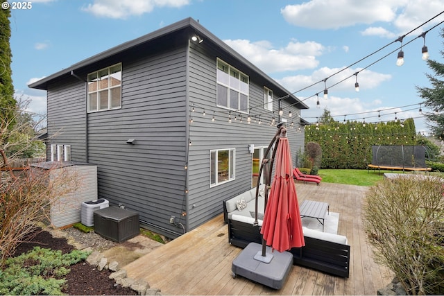 rear view of property with central AC unit, a wooden deck, outdoor lounge area, and a trampoline