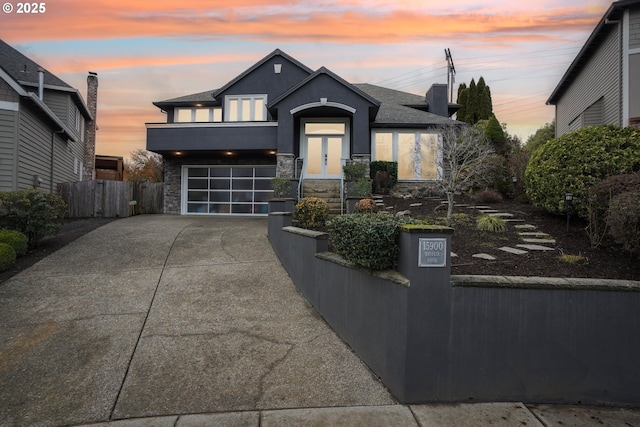 view of front of house with stone siding, a garage, fence, a balcony, and driveway