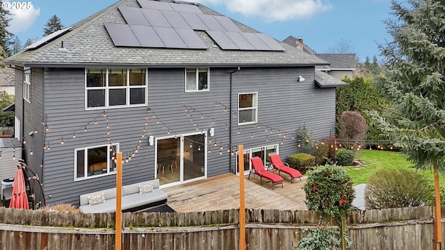 rear view of house featuring a chimney, fence, solar panels, and a wooden deck
