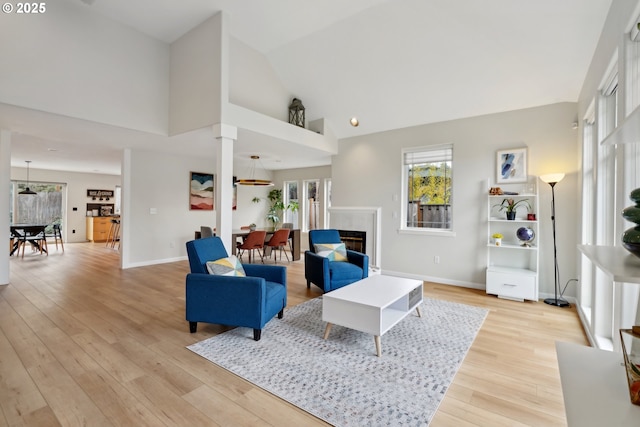 living area featuring high vaulted ceiling, a glass covered fireplace, light wood-style floors, and baseboards