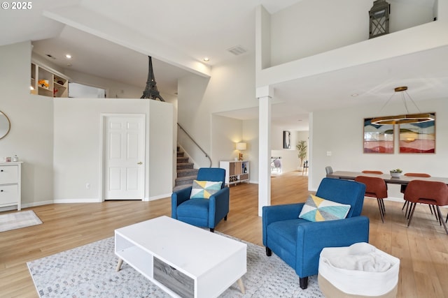 living area with high vaulted ceiling, decorative columns, visible vents, wood finished floors, and stairs