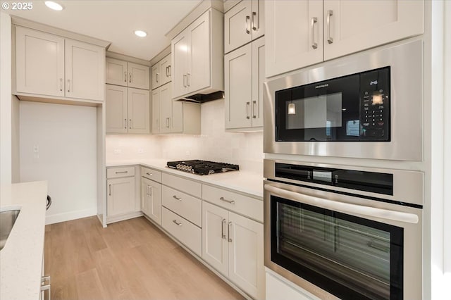 kitchen with decorative backsplash, light stone counters, stainless steel appliances, and light hardwood / wood-style flooring