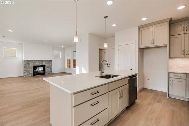 kitchen featuring dishwasher, a kitchen island with sink, hanging light fixtures, sink, and a fireplace