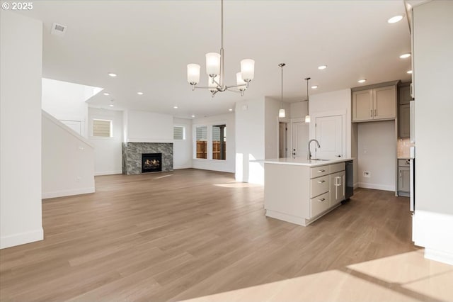 kitchen featuring a high end fireplace, gray cabinetry, a kitchen island with sink, decorative light fixtures, and light hardwood / wood-style flooring