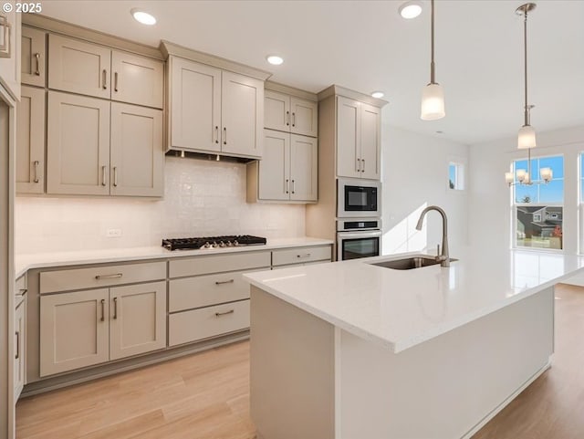 kitchen featuring a center island with sink, sink, hanging light fixtures, and stainless steel appliances