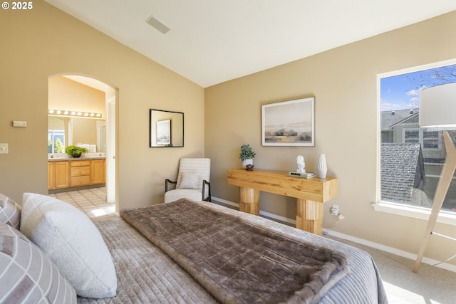 bedroom featuring arched walkways, lofted ceiling, ensuite bathroom, light carpet, and baseboards