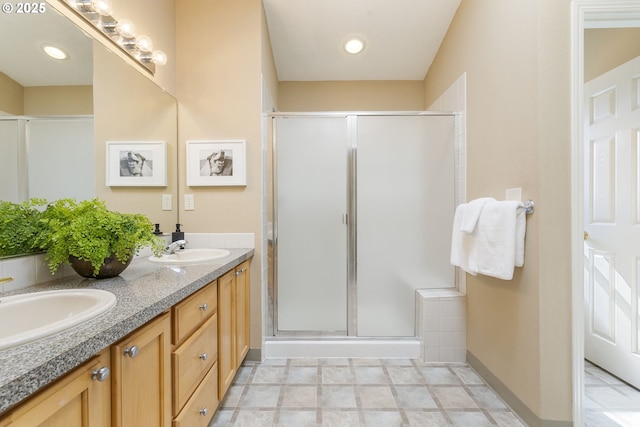 bathroom with baseboards, double vanity, a sink, and a shower stall