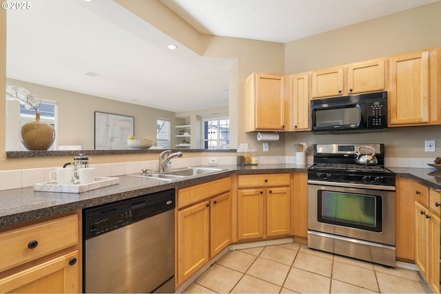 kitchen featuring appliances with stainless steel finishes, dark countertops, a sink, and light brown cabinetry