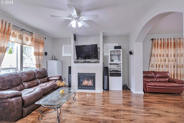 3963 NW 148th Pl, Portland, OR 97229 - living room with arched walkways, wood finished floors, a ceiling fan, a tile fireplace, and baseboards