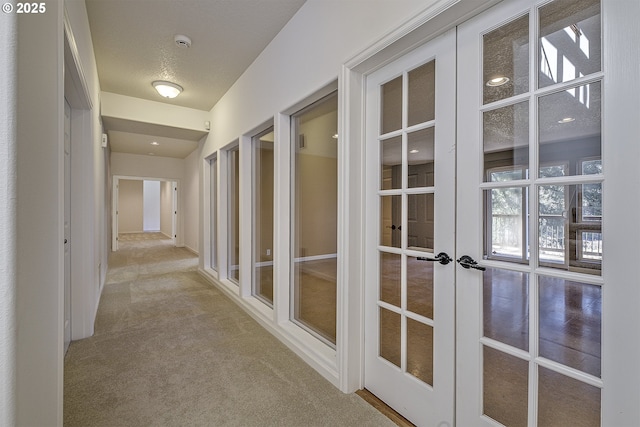 hall featuring french doors, carpet flooring, and a textured ceiling