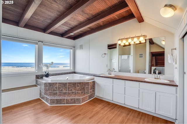 bathroom with lofted ceiling with beams, hardwood / wood-style flooring, a relaxing tiled tub, toilet, and a water view